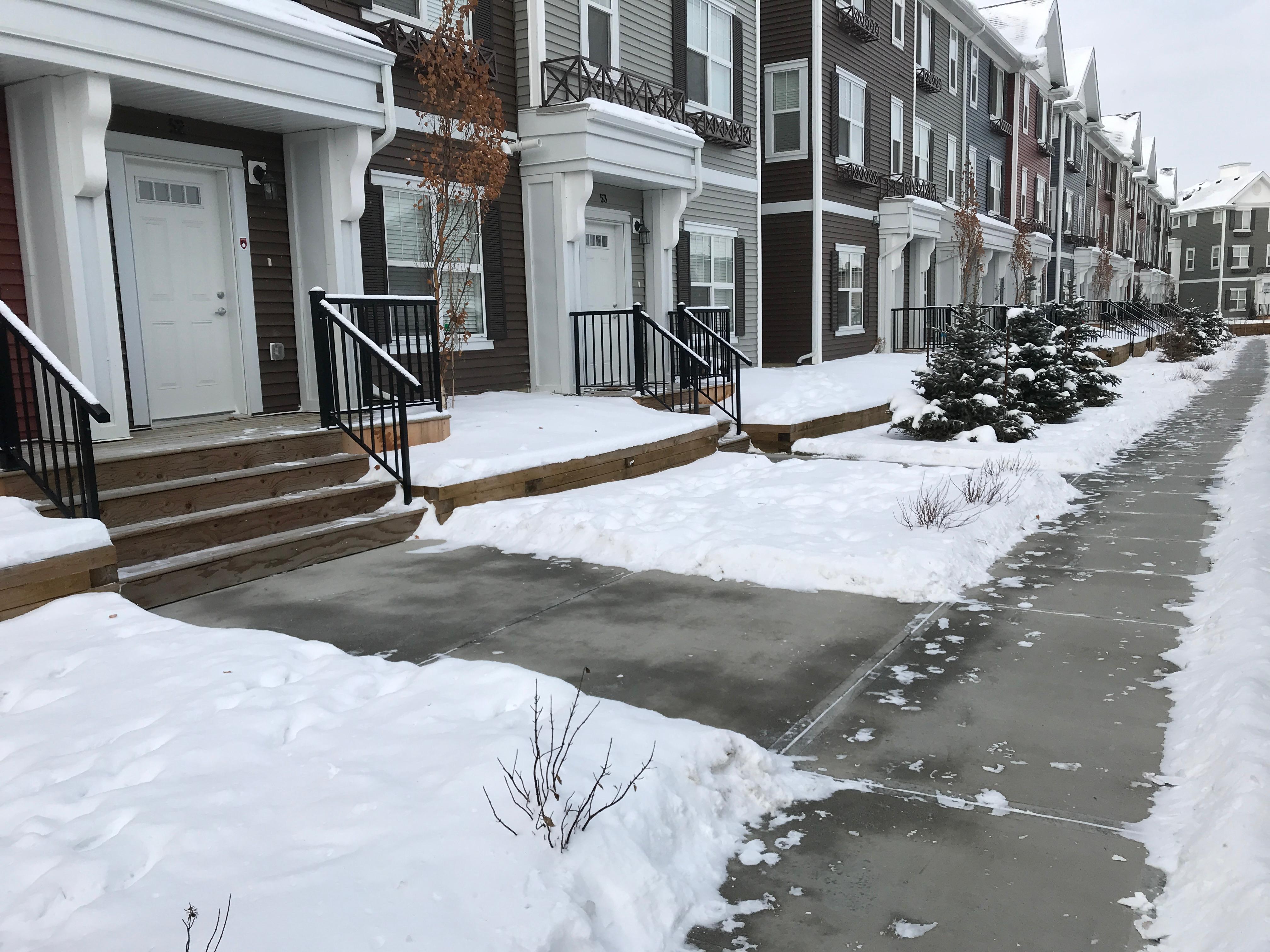 Row of townhouses with cleared front walkways and driveways in winter